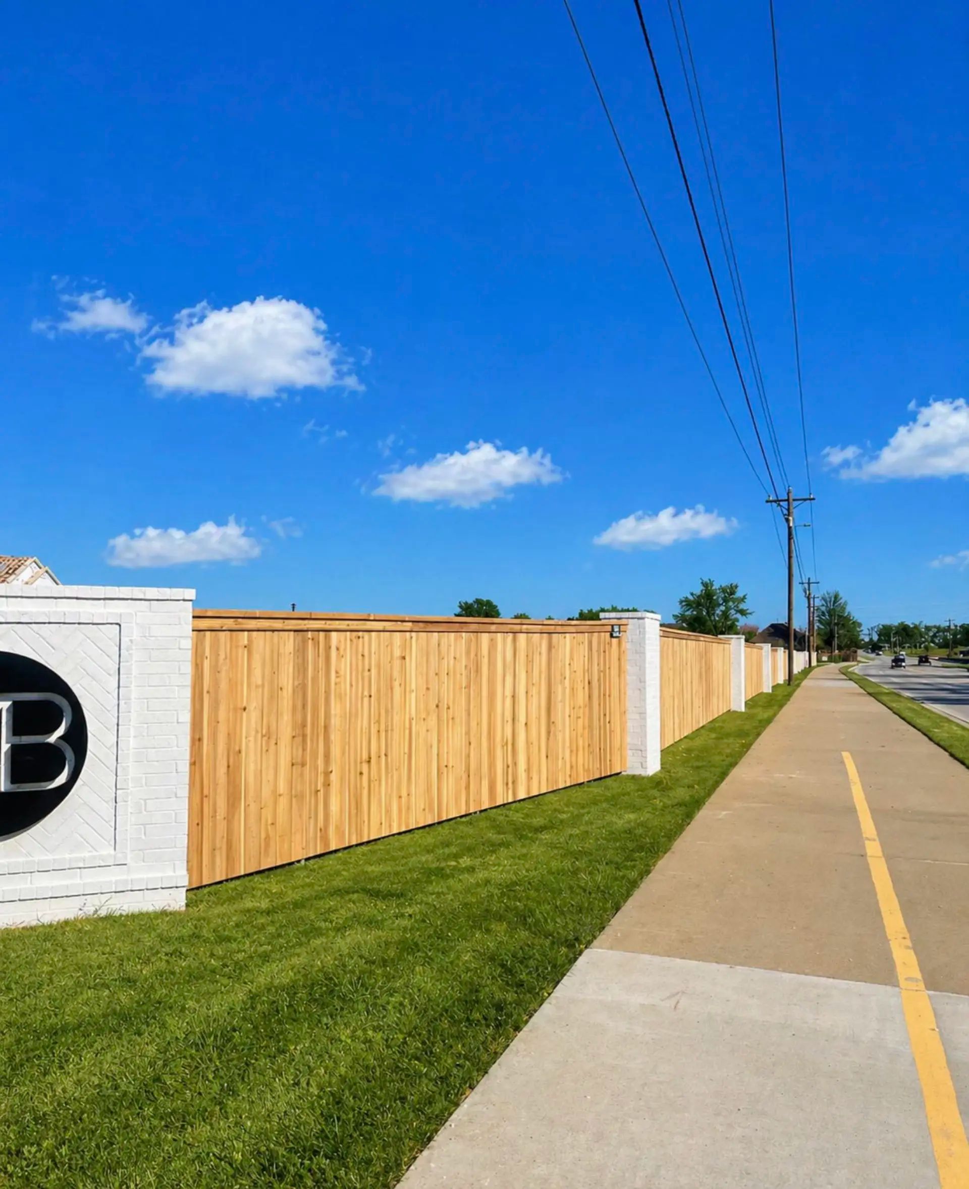 Subdivision perimeter fence featuring cedar pickets with cap and trim, metal posts, and white-painted brick columns.