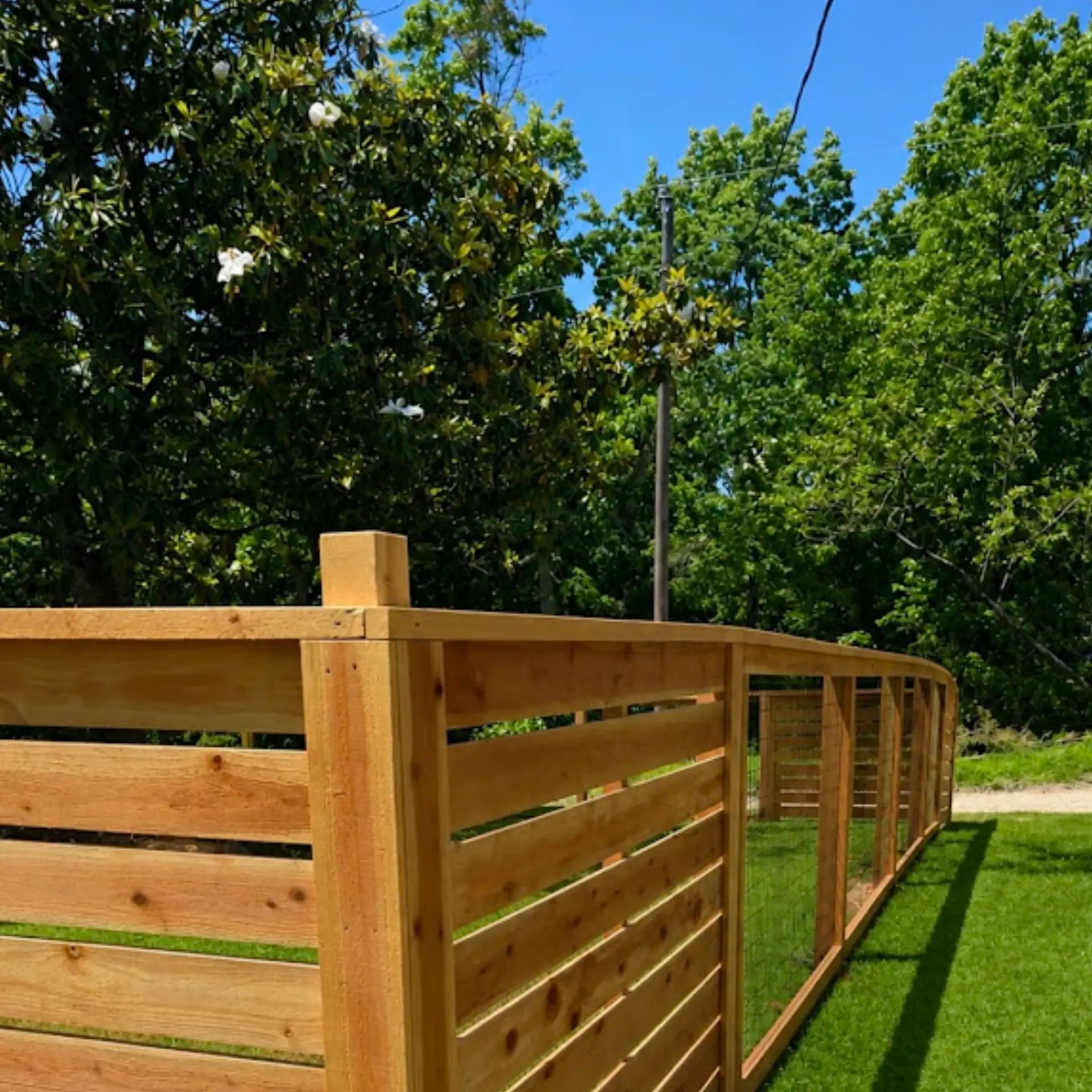 Custom 5-foot-tall open view redwood fence with black wire mesh panels and horizontal redwood accent sections in Rogers, Arkansas.